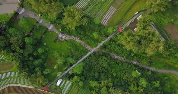 Vertical drone shot of river with waterfall metal with suspension bridge on it, surrounded by trees