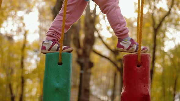 Little Child Make Steps and Balancing on Swinging Wooden Stump in Rope Park