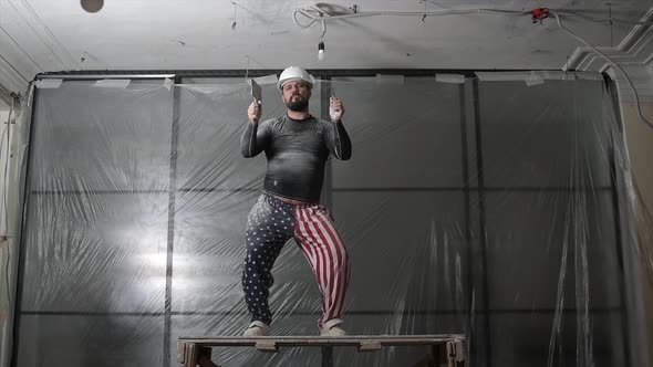 Fat Bearded Adult Man in Protective Helmet and USA Flag Print on Pants Remove Construction Whitewash