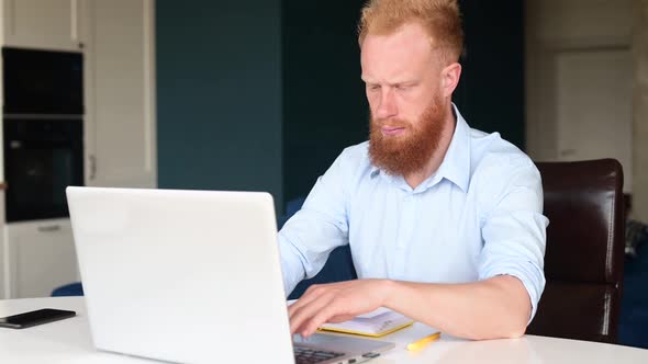 Absorbed and Thoughtful Red Haired Businessman Staring at the Computer Monitor