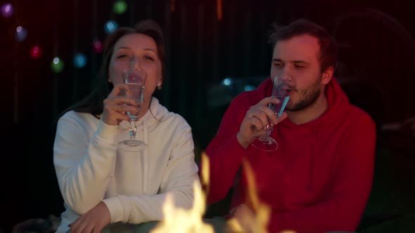 Happy Couple Relaxing Near a Fire and Drinking Champagne on a Summer Night