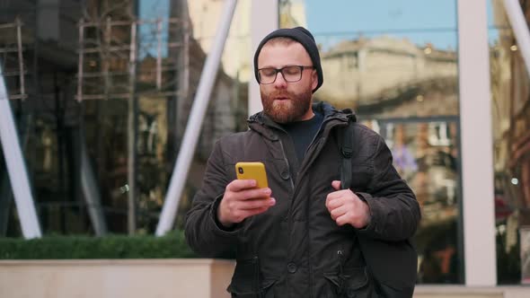Bearded Man in Glasses Making Shocked Face and Looking Disappointed While Using Smartphone. Serious