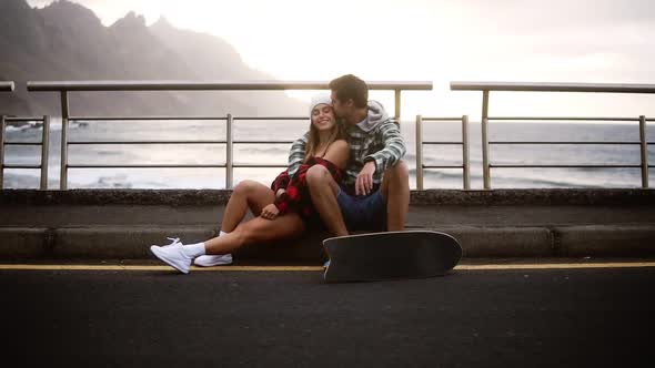 Loving Sport Couple Sitting on Border at Coastline Asphalt Road on Background Hills and Foggy Ocean