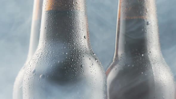 Three very cold beer bottles and smoke rotating on black background. Close up