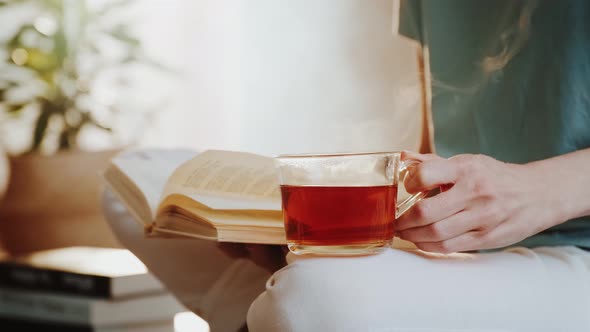 Woman Holding Steaming Cup of Tea or Coffee and Reading a Book.