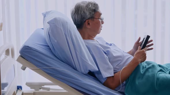 Elderly man holding photo frame with picture of family while lying on patient bed