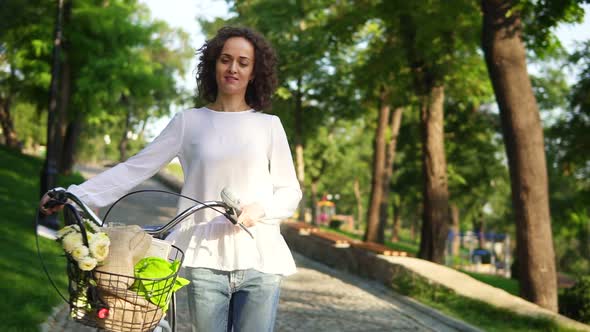 Young Woman in a White Tshirt and Blue Jeans Walking Holding Her City Bicycle's Handlebar with