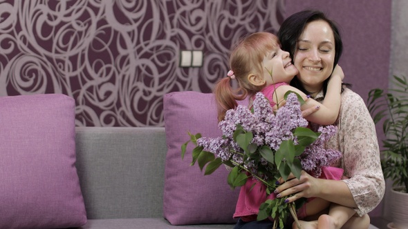 Little Daughter Child Congratulates Her Mother with Bouquet of Lilac Flowers