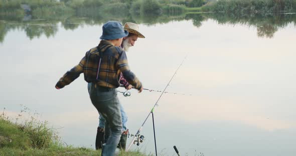 Grandfather Fishing Near the Pond and Calling His Interested Small Grandson