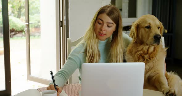 Woman writing on notepad with her dog at home 4k