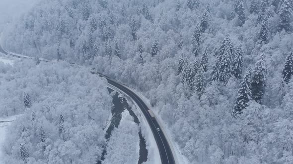 Aerial shot: cars and trucks are driving by the road in winter forest.