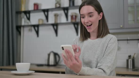 Young Woman Celebrating Success on Smartphone at Home