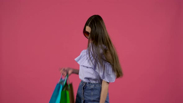 Girl in Sunglasses Dancing with Packages in Their Hands. Pink Background