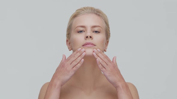 Studio portrait of young, beautiful and natural blond woman applying skin care cream. F