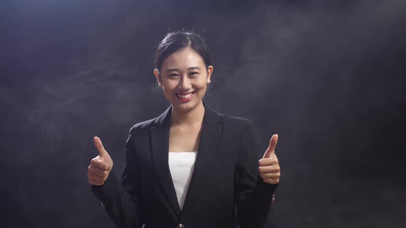 Smiling Asian Speaker Woman Showing Thumbs Up Gesture To Camera While Standing In The Black Studio