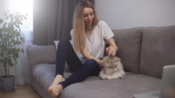 Young Woman Sitting on a Sofa Caresses a Tabby Cat