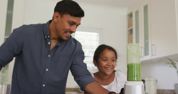 Hispanic father with smiling daughter teaching making smoothie in blender