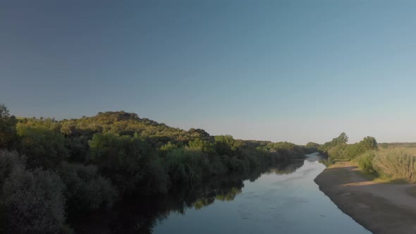 Drone shot of a calm river surrounded by trees during sunset