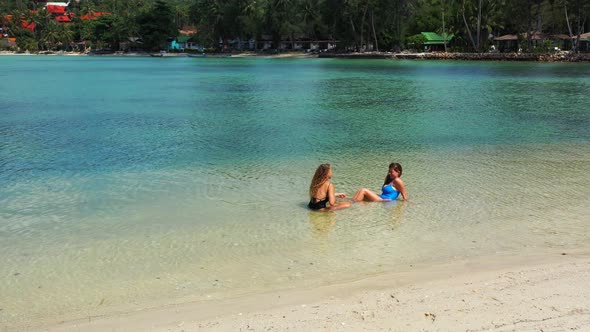 Young smiling girls on photoshoot in the sun at the beach on paradise white sand and blue background