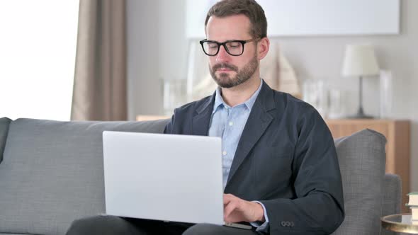 Young Businessman with Laptop Looking at Camera at Home 