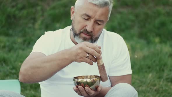 Man Holding a Bowl and a Wooden Stick Sitting in a Park