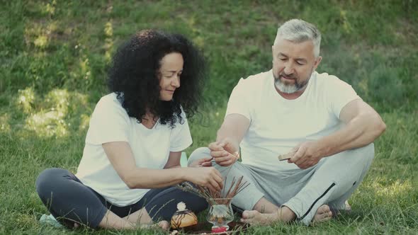 Healthy Man and Woman Are Sitting on the Grass and Preparing for Meditation Aroma Sticks