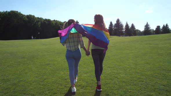 Lesbian Couple with Rainbow Flag Walking on Grass