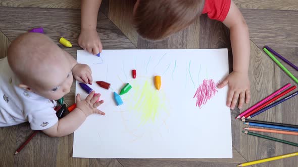 Baby Infant Lying on the Floor and Playing with Crayons While Little Boy Drawing