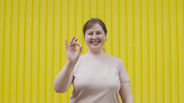 Woman Confidently Shows Gesture Ok at the Camera Near Yellow Wall