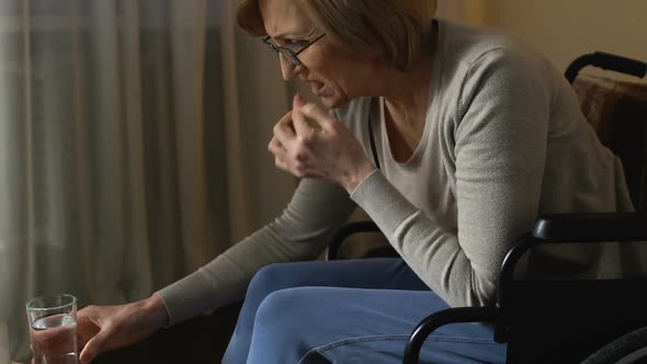 Sick Old Woman in Wheelchair Taking Pills Before Bedtime From Table in Hospital