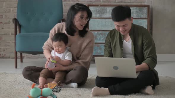 Young Asian family feeds baby son milk from bottle