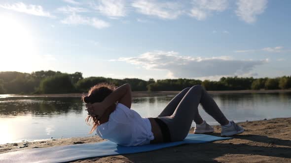 Woman Doing Sports Exercises, Shakes the Press at a Beautiful Sunset on the Beach, Sun Glare From