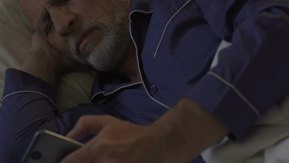 Aged Man Lying in Bed Awake at Night Scrolling Mobile Phone, Problems with Sleep
