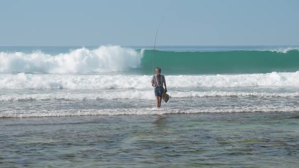 Local Fisherman Holds Rod in Hand in Waving Blue Ocean