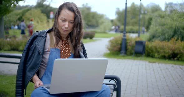 Young Townswoman Is Browsing Notebook Outside, Sitting on Bench in Park Area