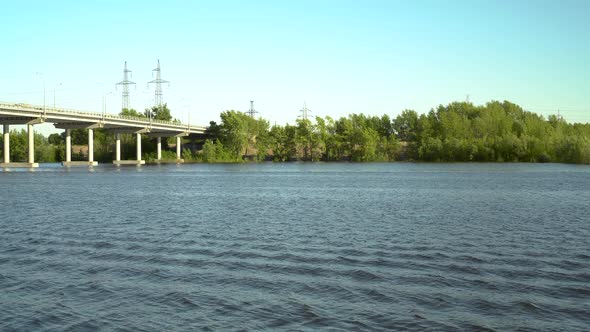 View of the Bridge Over the River. Blue River on a Background of Green Trees. A Bridge for the