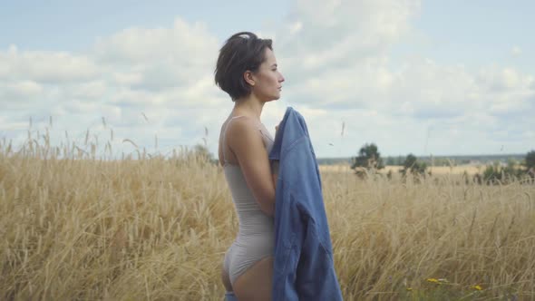 Side View of an Attractive Woman Wearing Bodysuit with Short Hair Holding Jeans Jacket on Her