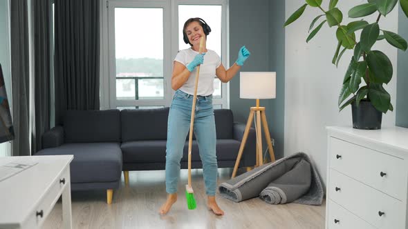 Woman in Headphones Cleans the House and Have Fun Singing with a Broom Like a Star at a Concert