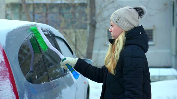 A Young Girl Brushes Her Car of Snow. Winter Morning Outdoors