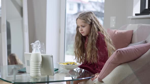 Happy Relaxed Girl Eating Morning Cereals Watching Cartoon on Tablet