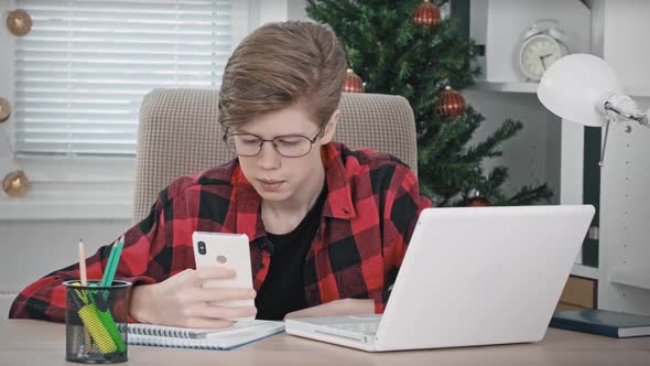 A Teenage Boy with Glasses is Carefully Studying the Information in His Phone Holding It in His