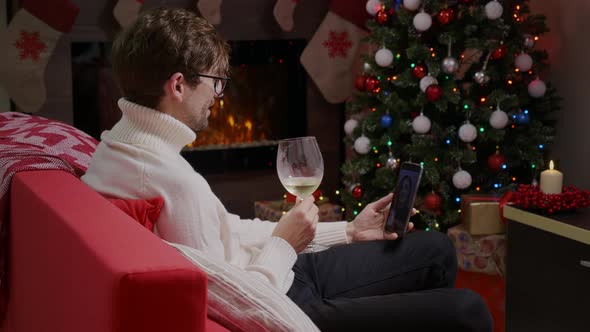 A young man having a video call on the phone and drinking some champagne on Christmas.