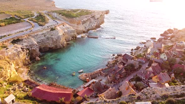 Small rocky cliff bay and small wooden town during golden sunset, aerial view