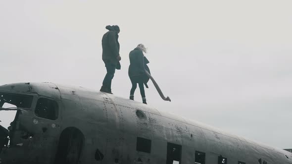 Young Traveling Couple Walking on the Top of Crashed DC-3 Plane in Iceland in the Windy Overcast Day