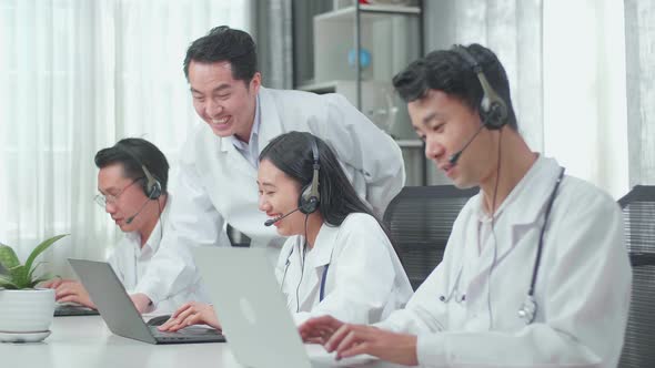 A Man Coming To Help A Woman Of Three Asian Doctors In Headsets Working As Call Centre Agent