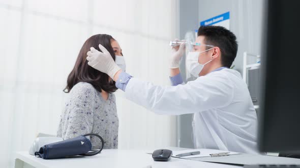 Asian specialist male doctor use flashlight on patient eye in hospital.