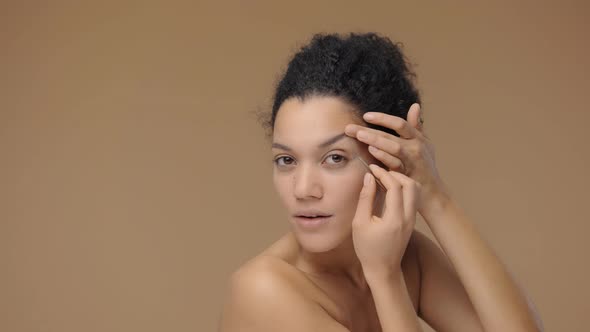 Beauty Portrait of Young African American Woman Looking in the Mirror and Plucking Her Eyebrows