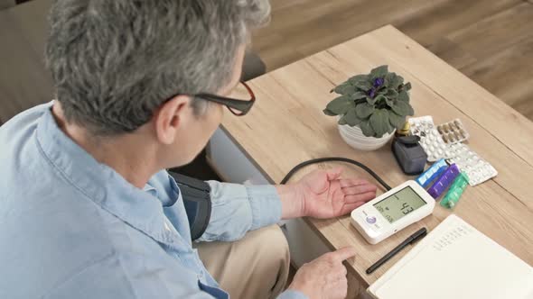 An Elderly Woman Measures Her Blood Pressure and Writes Down the Results in a Notebook