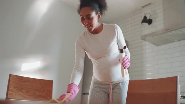 Positive African pregnant woman wiping the table with a damp cloth