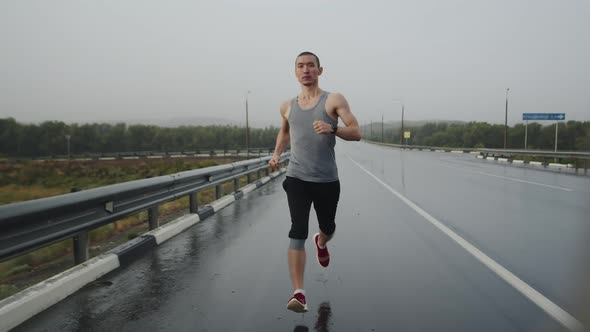 Asian Sports Triathlete Runs Marathon on Highway During Rain Front View
